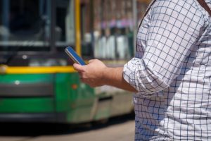 mies katsoo puhelinta ja taustalla raitiovaunu