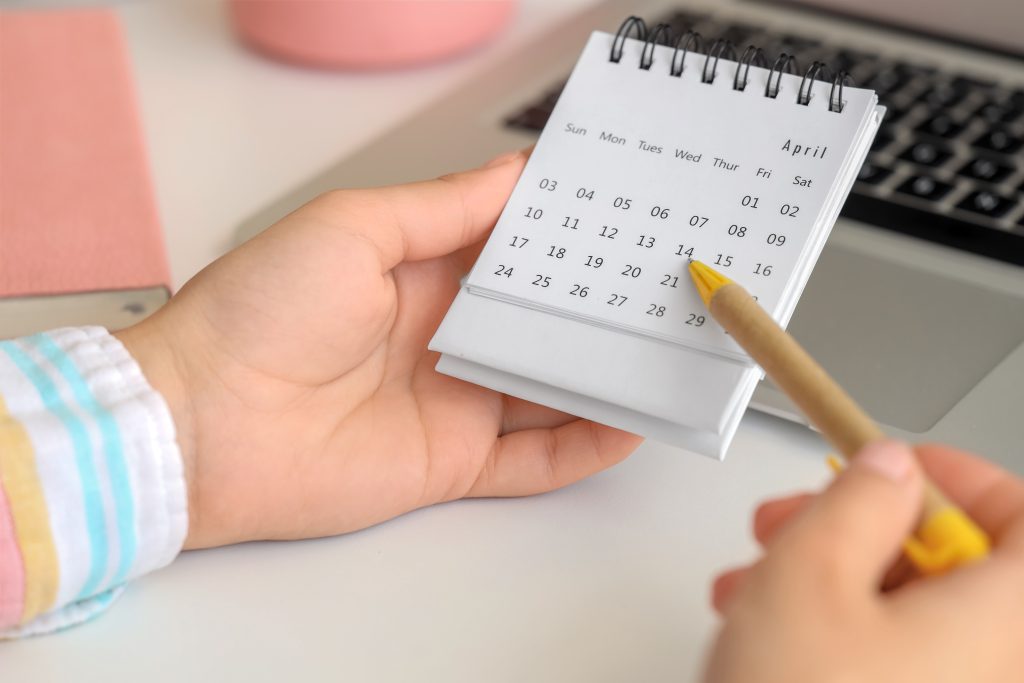 Kuvassa on kalenteri, johon henkilö on merkitsemässä kynällä. Vain henkilön kädet näkyvät.