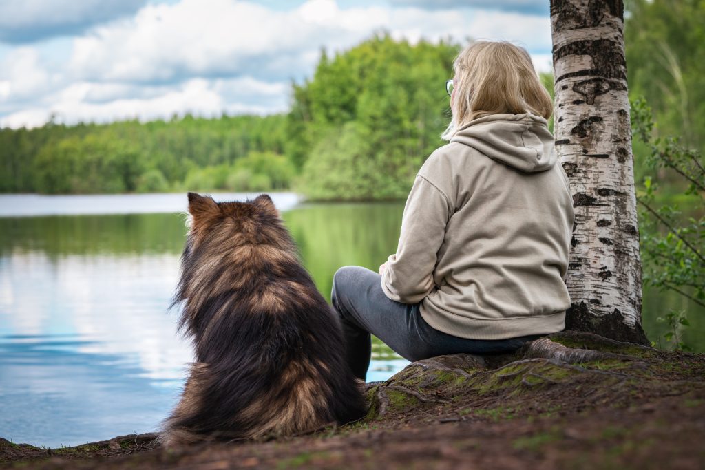Nainen istuu koiran kanssa järven rannalla