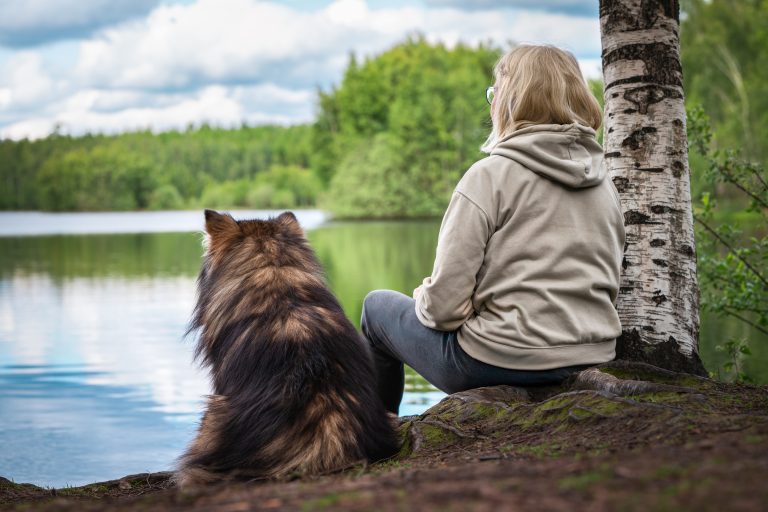 Nainen istuu koiran kanssa järven rannalla