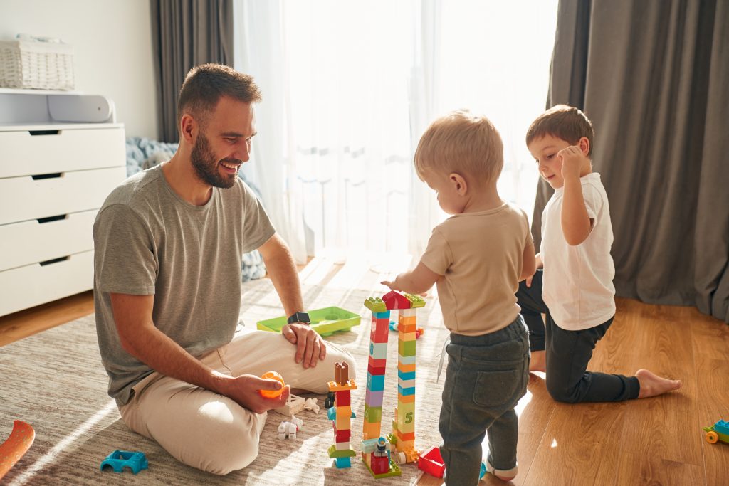 Isä leikkii kahden pienen lapsen kanssa. He rakentavat legoista torneja.