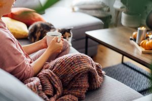 Lähikuva naisesta, joka istuu sohvalla kahvikuppi käsissään. Hänen vieressään sohvalla on kissa.